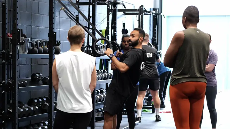 A coach guiding members through ring rows during a Hōm small group session