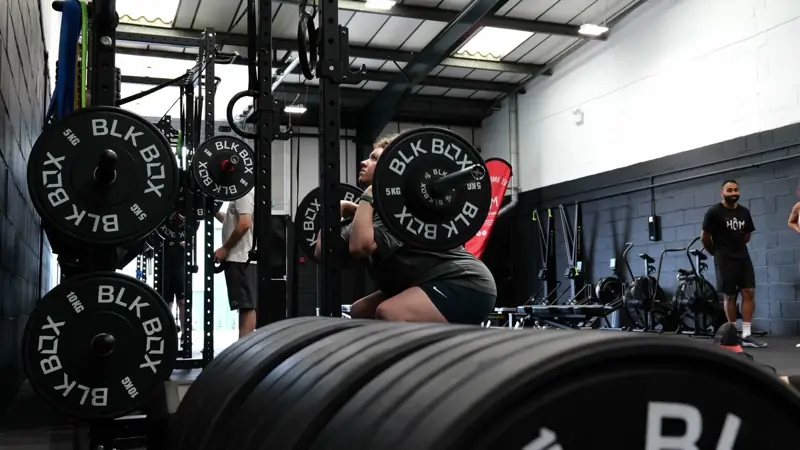 A member squatting with BLK BOX plates in a rack at Hōm